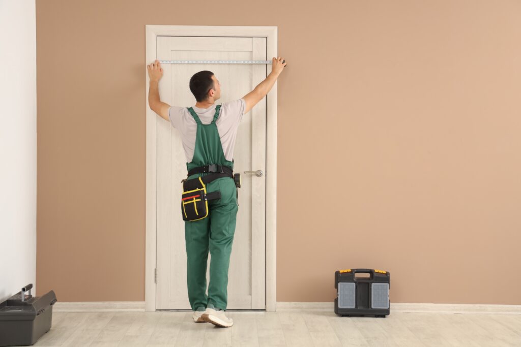 Guy in green overalls measuring a door